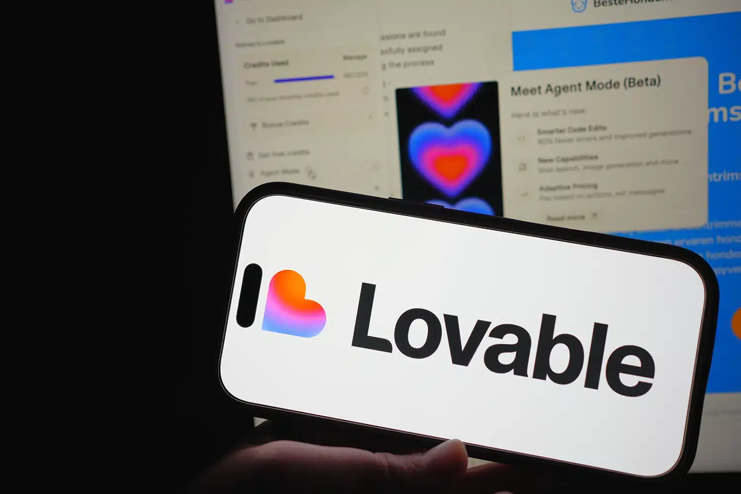 A smartphone showing the Lovable logo with its web platform for app building in the background.